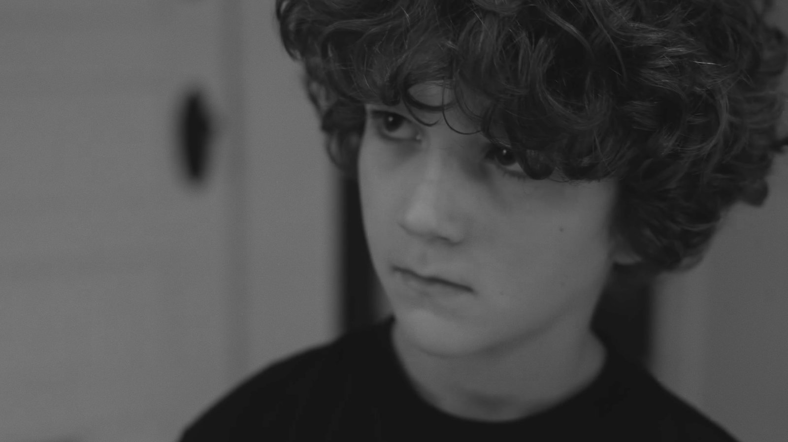 Black-and-white close-up of a curly-haired boy with a wary, downcast expression