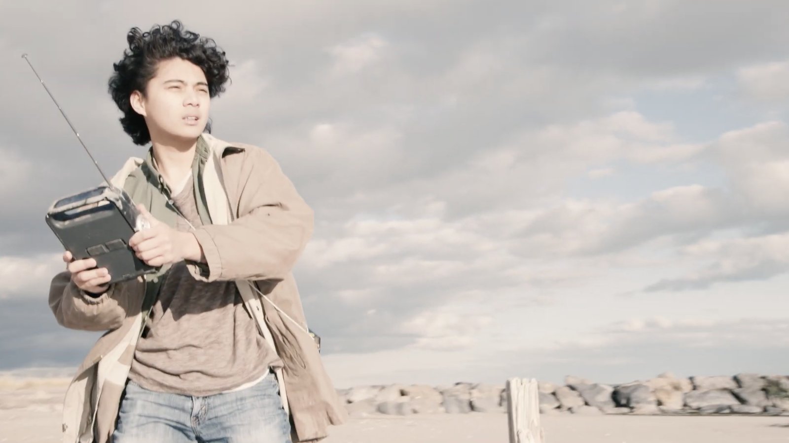 A young man clutches an old portable radio in a barren, windswept landscape
